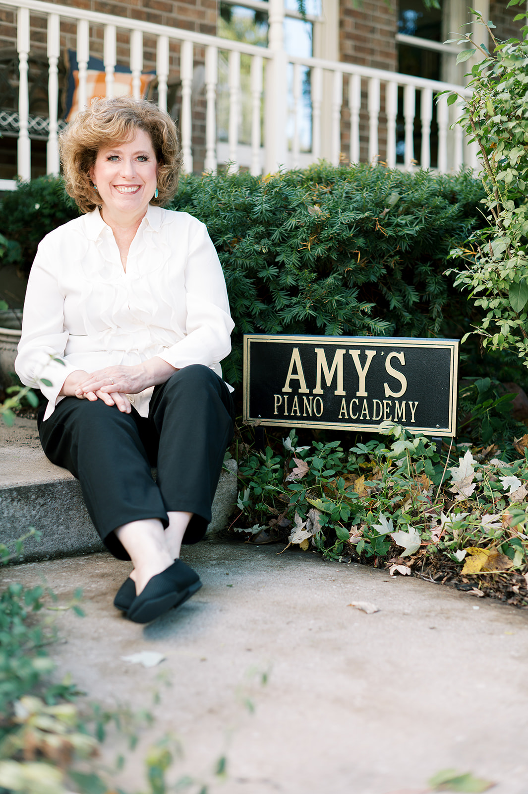 Amy sitting outside next to a sign reading 'Amy's Piano Academy'